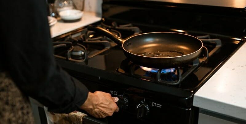 Woman cooking with frying pan on gas powered stove