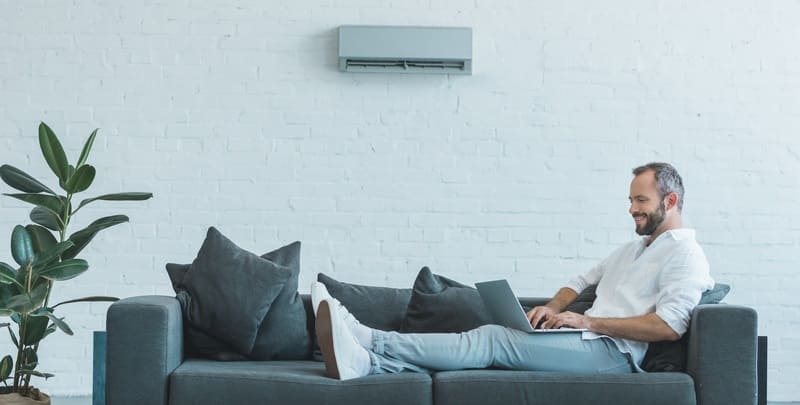 Man relaxing on couch with laptop while air conditioner is on